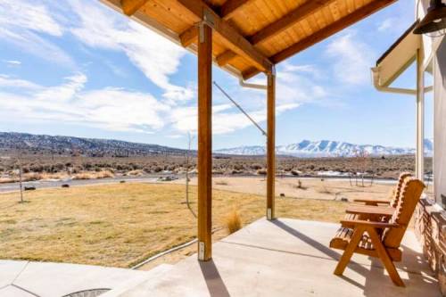 A scenic view from a porch with wooden chairs, overlooking a vast landscape and mountains under a blue sky.