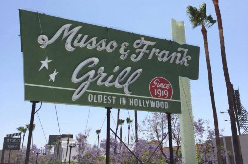 Sign for Musso & Frank Grill, the oldest restaurant in Hollywood, established in 1919, with palm trees in the background.
