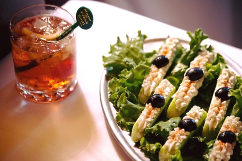 A plate of lettuce wraps with creamy filling and olives, alongside a glass of a dark cocktail with ice.