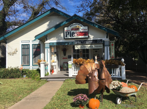 A charming house with a sign for a pie shop, decorated with autumn leaves, pumpkins, and a metal turkey sculpture.