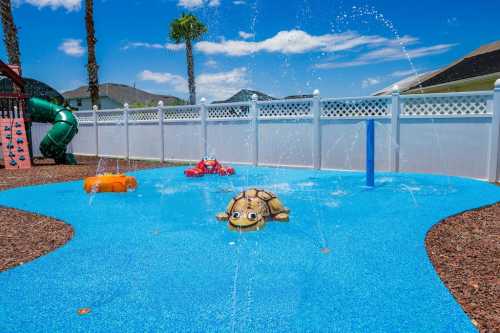 Colorful splash pad with a turtle feature, water sprays, and play structures under a clear blue sky.