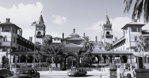 Historic building with towers and palm trees, featuring an arched entrance and flags, in black and white.