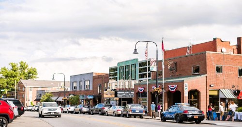 A bustling downtown street with shops, a theater, and parked cars under a cloudy sky.