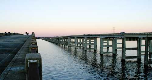 A long bridge stretches over calm water, reflecting the pastel colors of the sky at dusk.