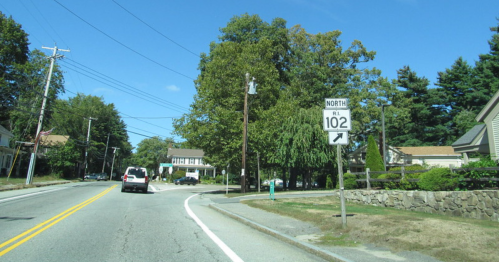 A road sign indicating Route 102 North, with houses and trees lining the street on a clear day.