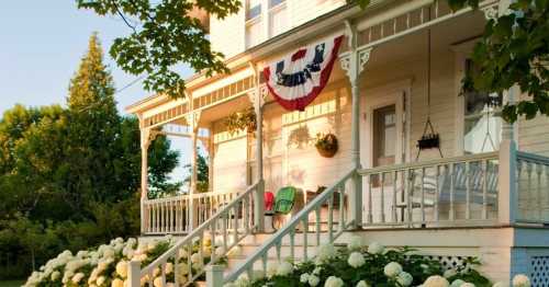 A charming white house with a porch, decorated with bunting and surrounded by blooming hydrangeas.