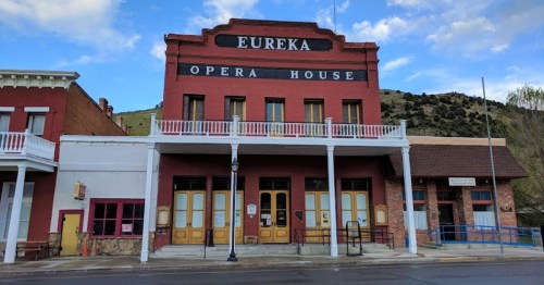 Historic Eureka Opera House with a red brick facade and white balcony, set against a mountainous backdrop.