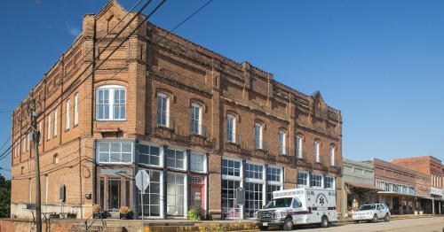 Historic brick buildings line a street under a clear blue sky, with an ambulance parked nearby.