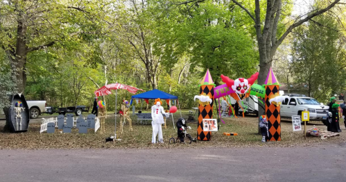 A festive Halloween scene with decorations, inflatables, and costumed figures in a wooded area.