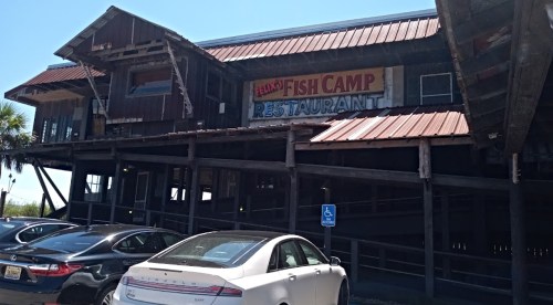 Exterior of Felix's Fish Camp Restaurant, a wooden building with a metal roof, surrounded by parked cars.