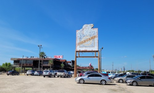 A seafood restaurant with a large sign reading "Fish Camp" and a busy parking lot under a clear blue sky.