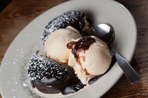 A plate with two chocolate-covered desserts and two scoops of vanilla ice cream drizzled with chocolate sauce.