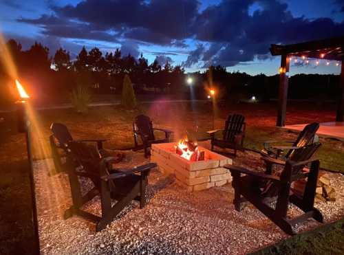 A cozy fire pit surrounded by black chairs, with a twilight sky and torches illuminating the scene.