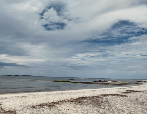 A serene beach scene with soft sand, calm water, and a cloudy sky in the background.