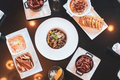 A table spread featuring a central bowl of stir-fried vegetables, surrounded by various appetizers and a drink.
