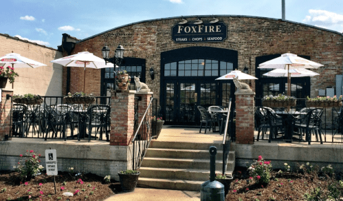 Exterior of FoxFire restaurant featuring outdoor seating, umbrellas, and a brick facade with flower planters.