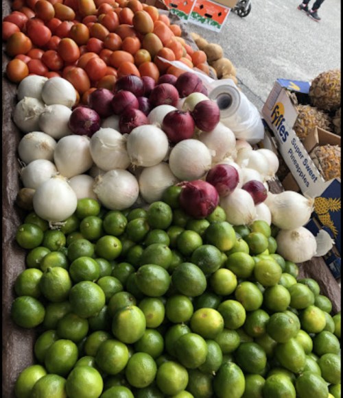 A vibrant display of fresh produce, including red and green tomatoes, white and red onions, and limes at a market.