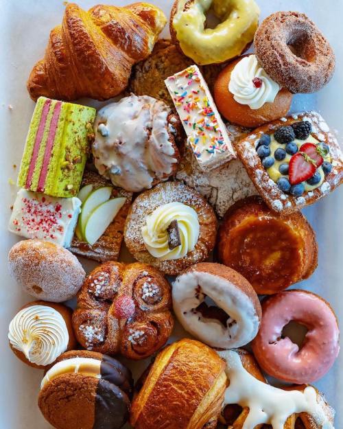 A colorful assortment of pastries, including donuts, croissants, and cakes, arranged on a white surface.