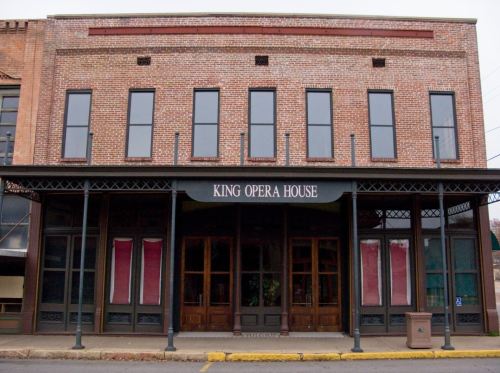 Historic brick building with large windows and a sign reading "King Opera House" at the entrance.