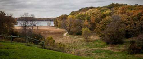 A scenic view of a lake surrounded by autumn trees and a winding path through a grassy area.