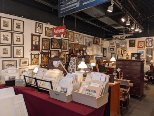 A cozy antique shop filled with framed pictures, vintage furniture, and decorative items, with customers browsing.