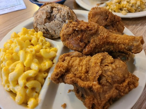 A plate of fried chicken, macaroni and cheese, and a cookie, served on a wooden table.