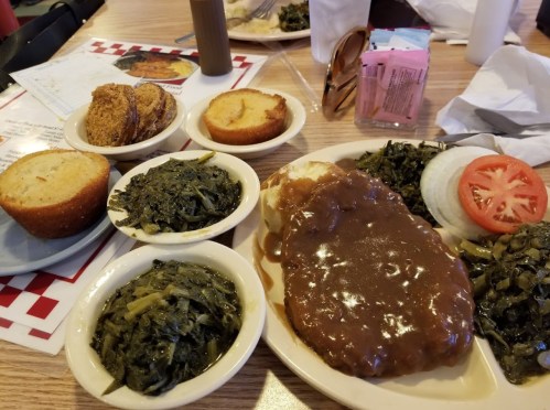A plate of meatloaf with gravy, served with collard greens, sliced tomatoes, and cornbread muffins on the side.