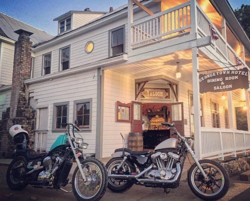 Two motorcycles parked in front of a historic building with a sign for the Georgetown Hotel and Saloon.