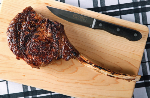 A perfectly cooked tomahawk steak on a wooden cutting board, accompanied by a sharp knife.