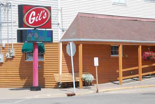 Sign for "Gil's" restaurant with a colorful display, wooden exterior, and a bench outside.