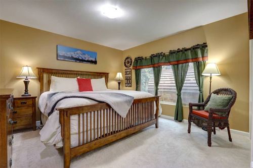 Cozy bedroom with a wooden bed, lamps, and green curtains, featuring a window and a wicker chair.