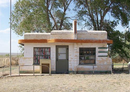 A small, weathered building with a flat roof, colorful windows, and surrounded by trees in a rural setting.