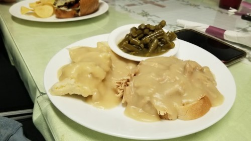 A plate of food featuring chicken and gravy over bread, served with green beans on the side.