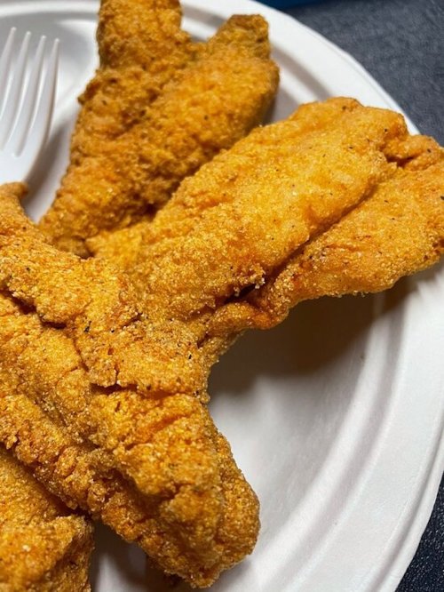 Three golden-brown, crispy fried fish fillets on a white paper plate.