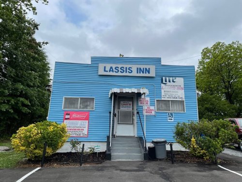 A blue building with a sign reading "Lassis Inn," surrounded by greenery and a cloudy sky.