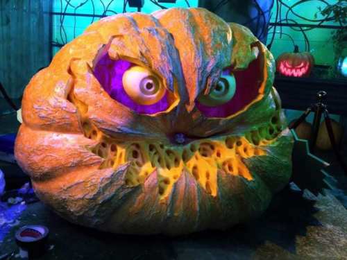 A large, menacing pumpkin with bulging eyes and a carved face, illuminated in colorful Halloween lights.