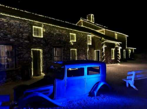 A stone building adorned with string lights at night, with a vintage car parked in front, illuminated by blue light.