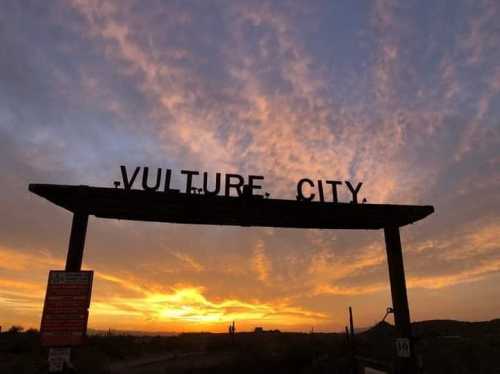 Sign reading "Vulture City" silhouetted against a colorful sunset sky.