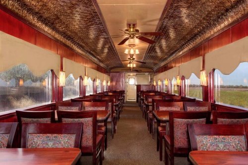 Interior of a vintage diner car with wooden tables, patterned chairs, and large windows, creating a cozy atmosphere.