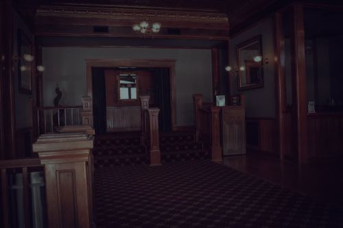 A dimly lit wooden foyer with a staircase, ornate lighting, and a large mirror reflecting the space.