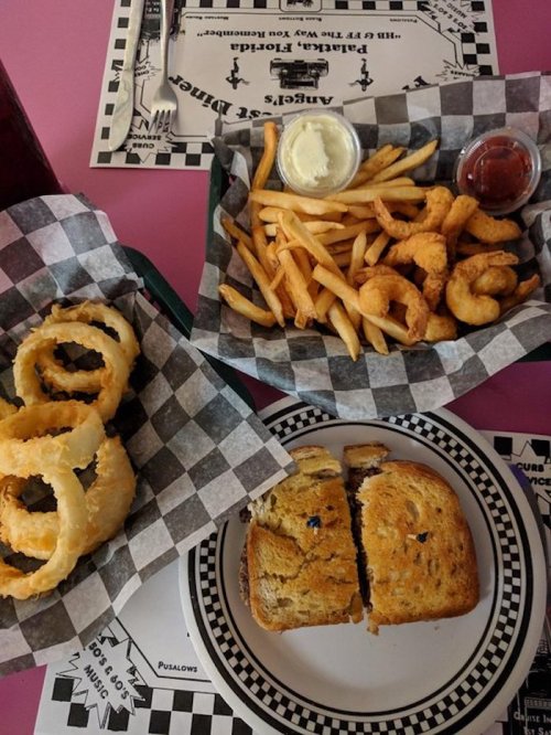 A plate of onion rings, a basket of fries and shrimp, and a sandwich on a checkered tablecloth.