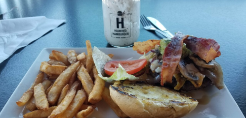 A plate with a burger topped with bacon, mushrooms, and lettuce, served with fries and a milkshake in the background.