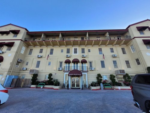 Front view of the Grand Hotel, featuring a yellow facade, multiple air conditioning units, and decorative plants.