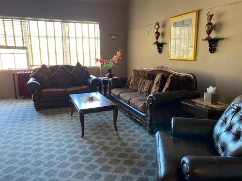 A cozy living room with two sofas, a coffee table, and decorative wall shelves, featuring large windows and floral accents.