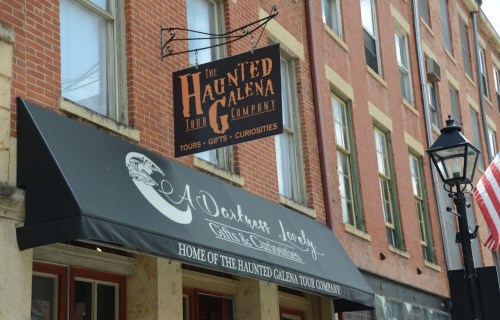 Sign for "The Haunted Galena Tour Company" above a storefront, featuring tours, gifts, and curiosities.