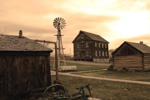 A rustic landscape featuring a windmill, wooden buildings, and a cloudy sunset sky.