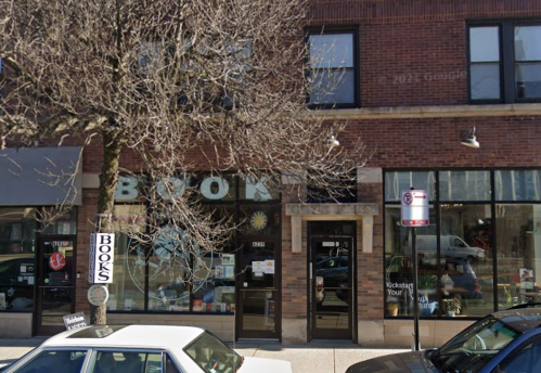 A brick storefront with large "BOOKS" sign, featuring a tree and parked car in front.