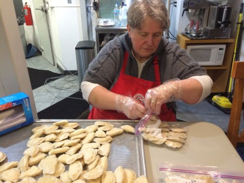 A woman in an apron bags homemade dumplings on a table, with a kitchen in the background.