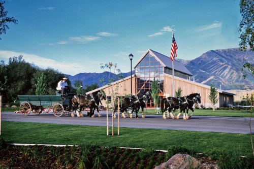 A horse-drawn carriage passes by a modern building with an American flag, set against a mountain backdrop.