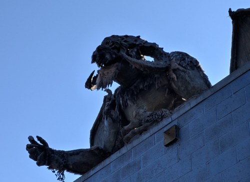 A large, weathered monster sculpture perched on a building, with a blue sky in the background.